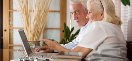 Two elderly people looking at a laptop and smiling.